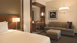 A hotel room with a large bed, a desk, a sofa, and a small ottoman.