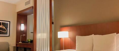 A hotel room with a large bed, a desk with a lamp, a chair, a large mirror, and a painting on the wall.