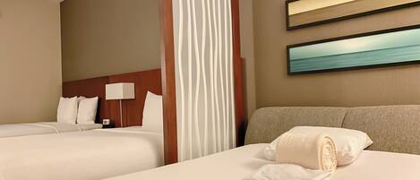 A hotel room with two beds, a wooden headboard, a nightstand with a lamp, and a painting on the wall.