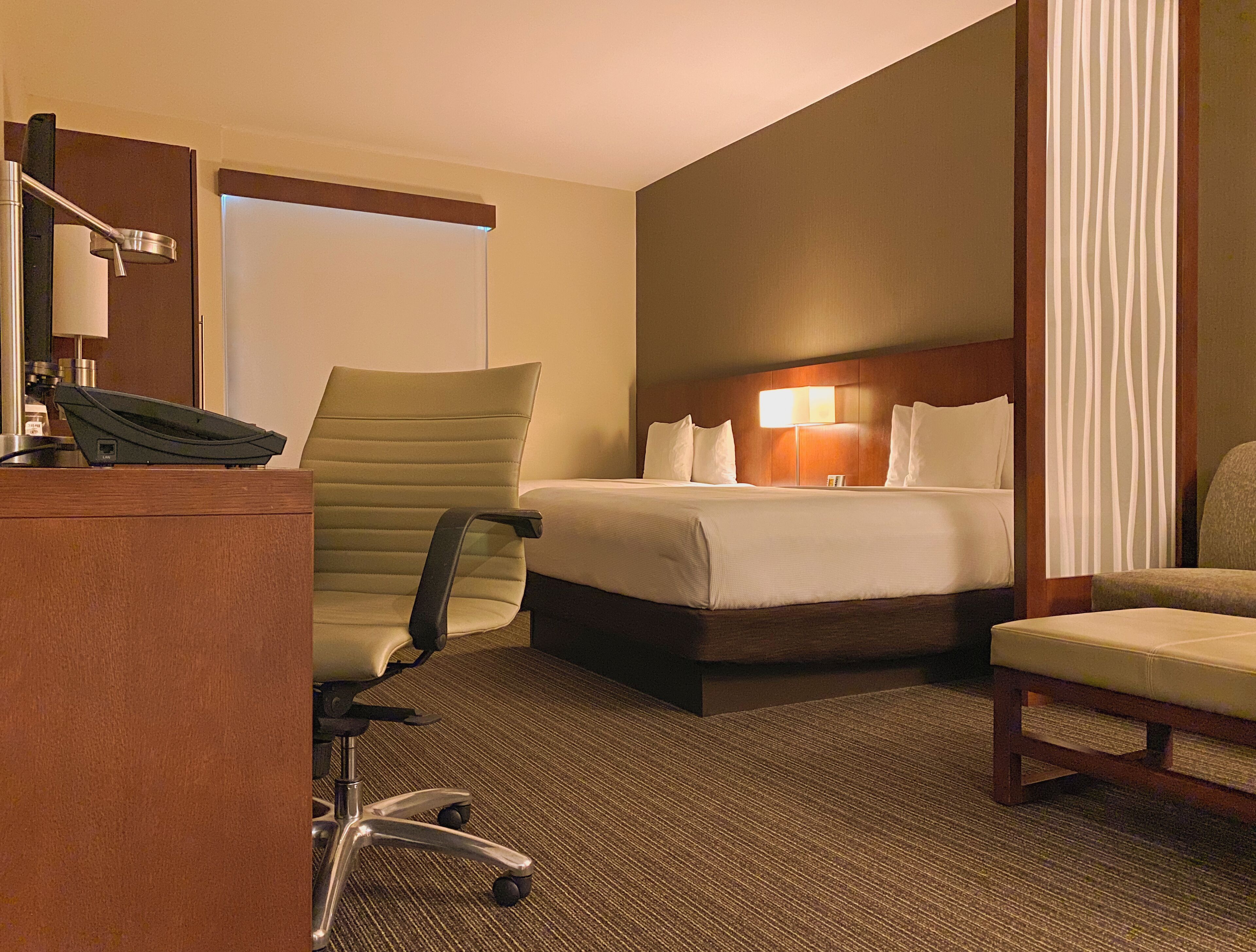 Habitación de hotel con cama, escritorio, teléfono, silla y lámpara.