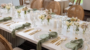A long dining table set with glassware, plates, and cutlery, surrounded by wicker chairs.