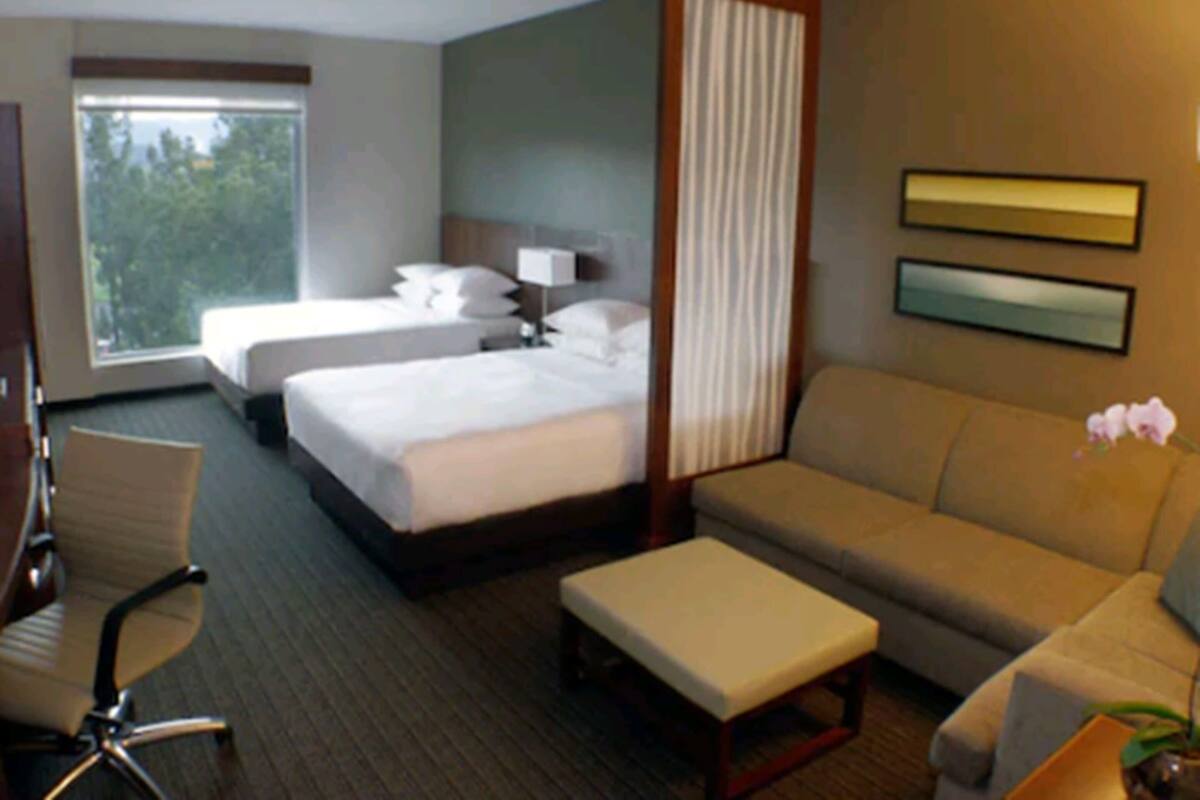Habitación de hotel con dos camas, un sofá, una silla, una mesita y ventana con vista a árboles.