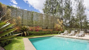 Una piscina con sillas de descanso, rodeada de follaje y árboles altos.