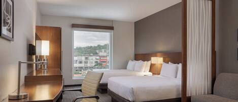A hotel room with two beds, a desk, a chair, a sofa, a window with a view, and a lamp.