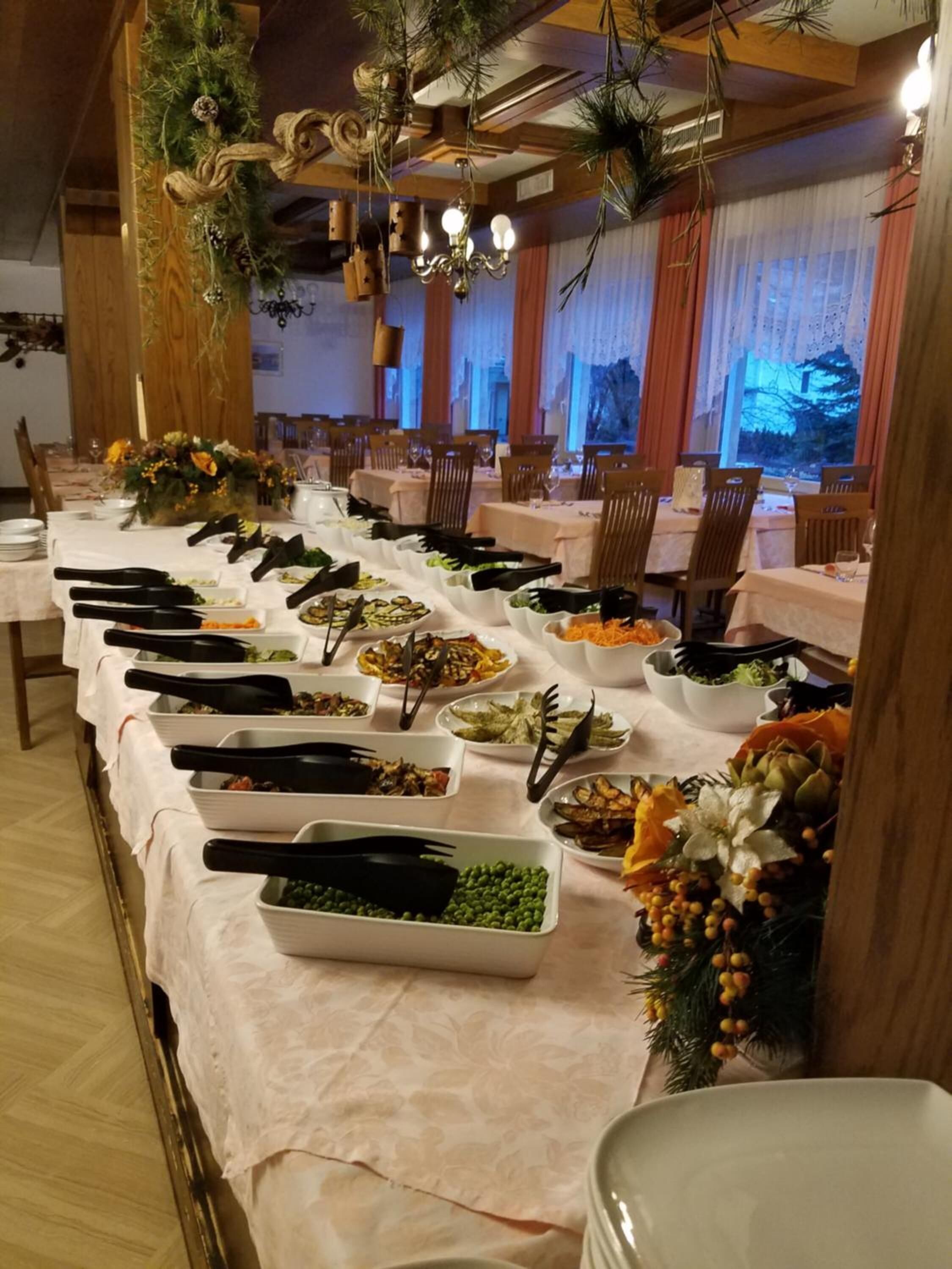 Un'imbandita tavola da buffet con diversi piatti e utensili da portata, circondata da sedie e un soffitto decorato.