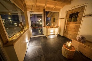 A wooden interior with a glass door leading outside, a small wooden stool with candles, and a bench with towels. - Bellaria (Predazzo)