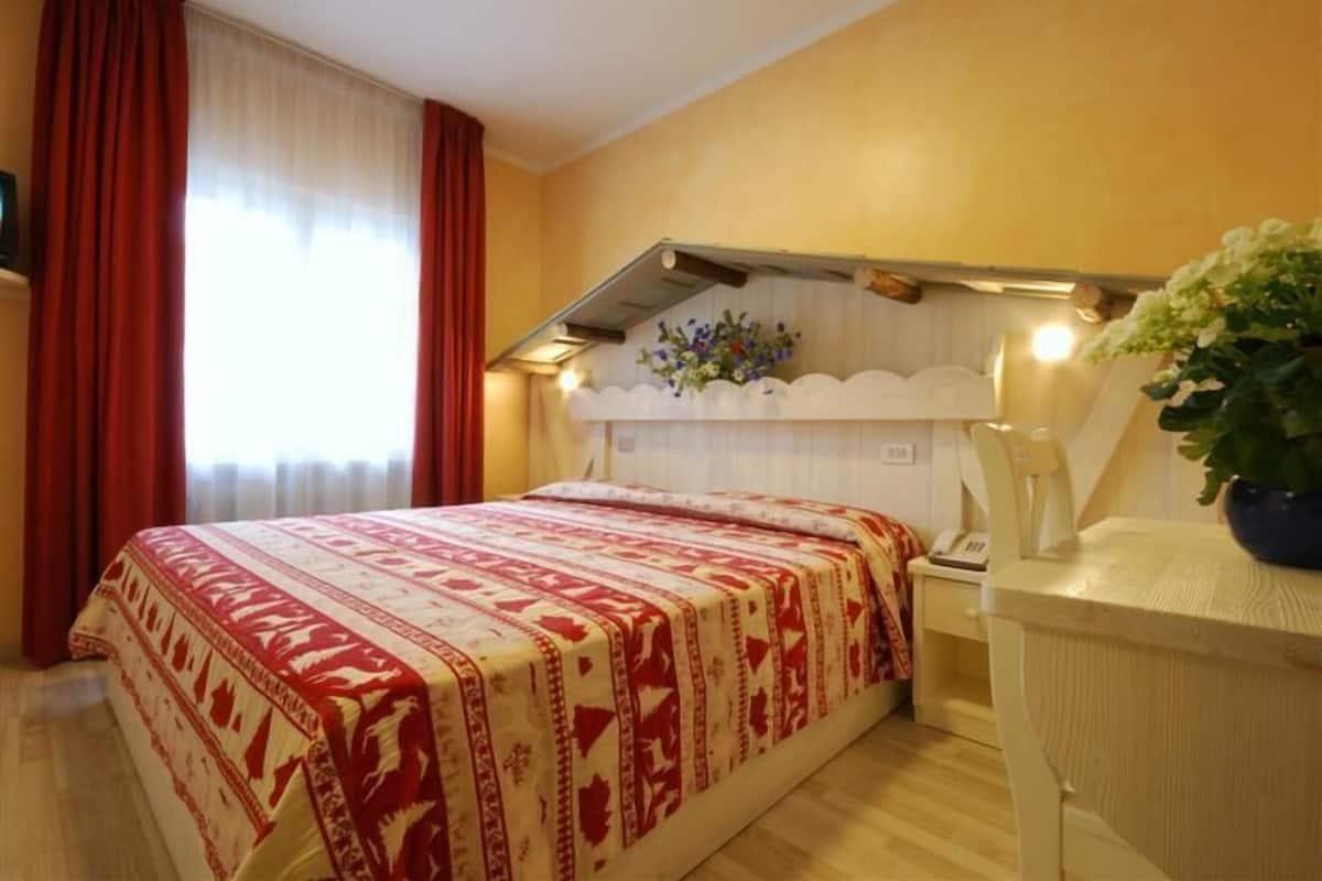 A hotel room with a bed, a nightstand, a desk, and a potted plant.
