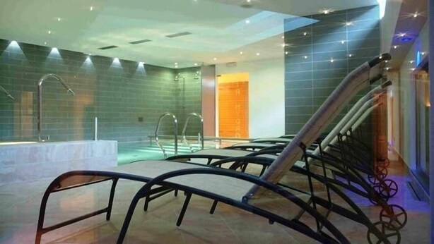A modern indoor pool area with clear glass walls, a central water feature, and a staircase with metal railings. - Bellaria (Predazzo)
