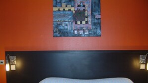 A bed with a patterned bedspread, a dark headboard, and two wall-mounted light fixtures. - La Siesta (Mont-de-Marsan)