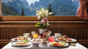 Une table de petit-déjeuner avec divers plats et un vase de fleurs, le tout mis en valeur par une vue sur les montagnes.