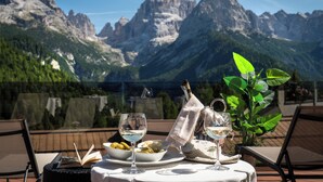 Une table dressée avec des verres à vin, une bouteille, des olives et du fromage, donnant sur un paysage montagneux.