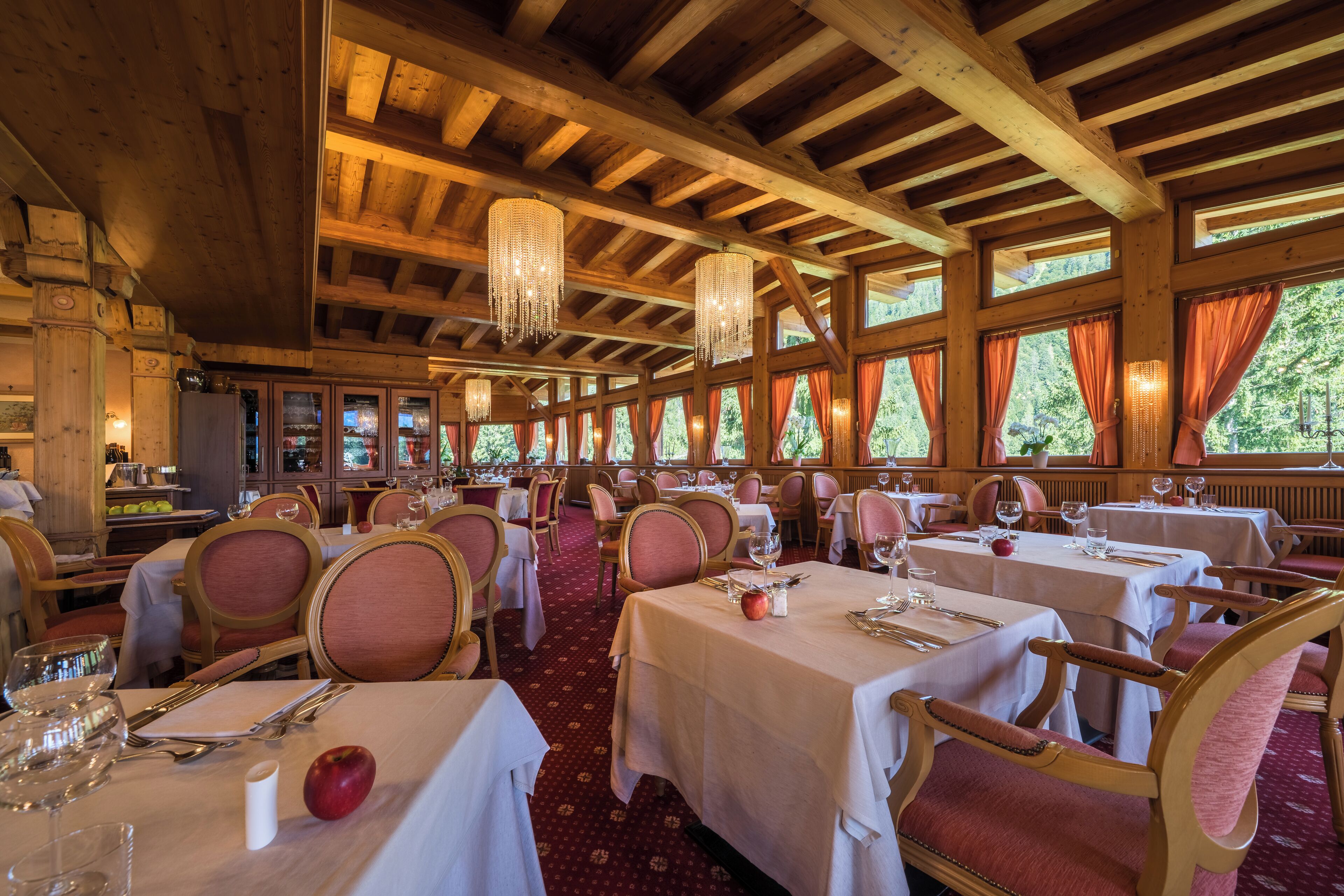 Een restaurant met houten balken en grote ramen, tafels gedekt met witte tafelkleden en rode stoelen.
