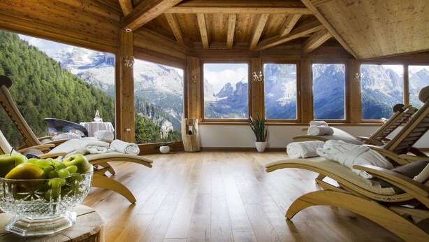 Un chalet en bois avec deux fauteuils inclinables, un saladier en verre rempli de fruits et une vue sur les montagnes.