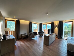 A spacious room with wooden flooring, a sofa, a chair, a TV, and a bed. - HOTEL LORENZETTI (Pinzolo)
