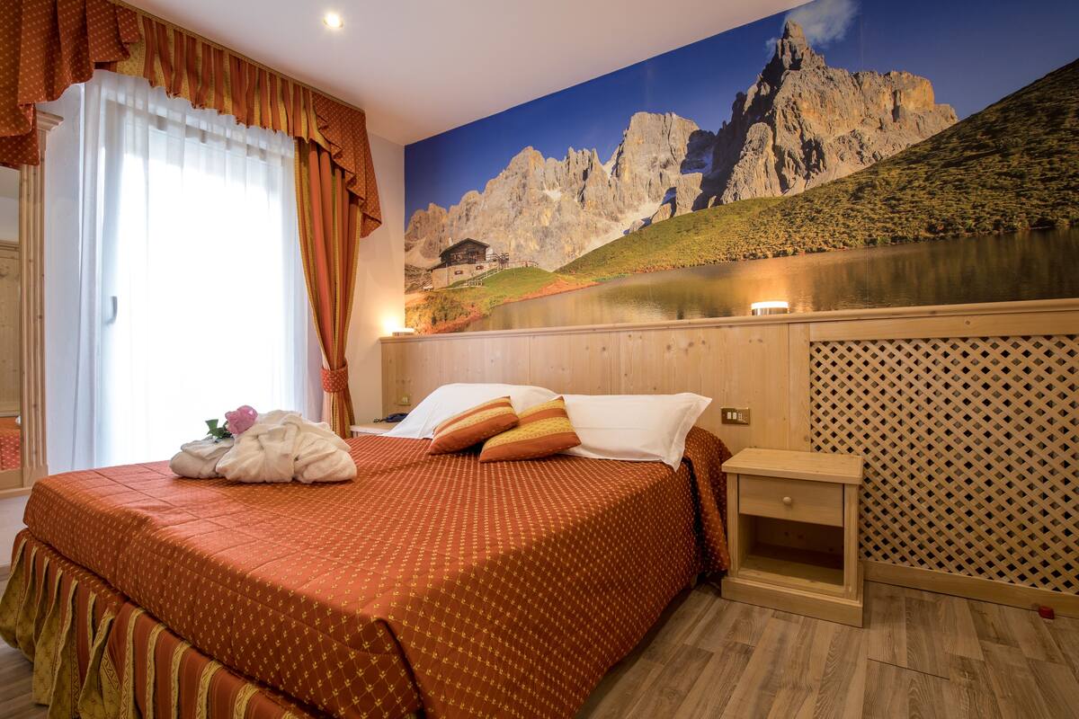 A hotel room with a bed, a nightstand, and a large window with curtains.