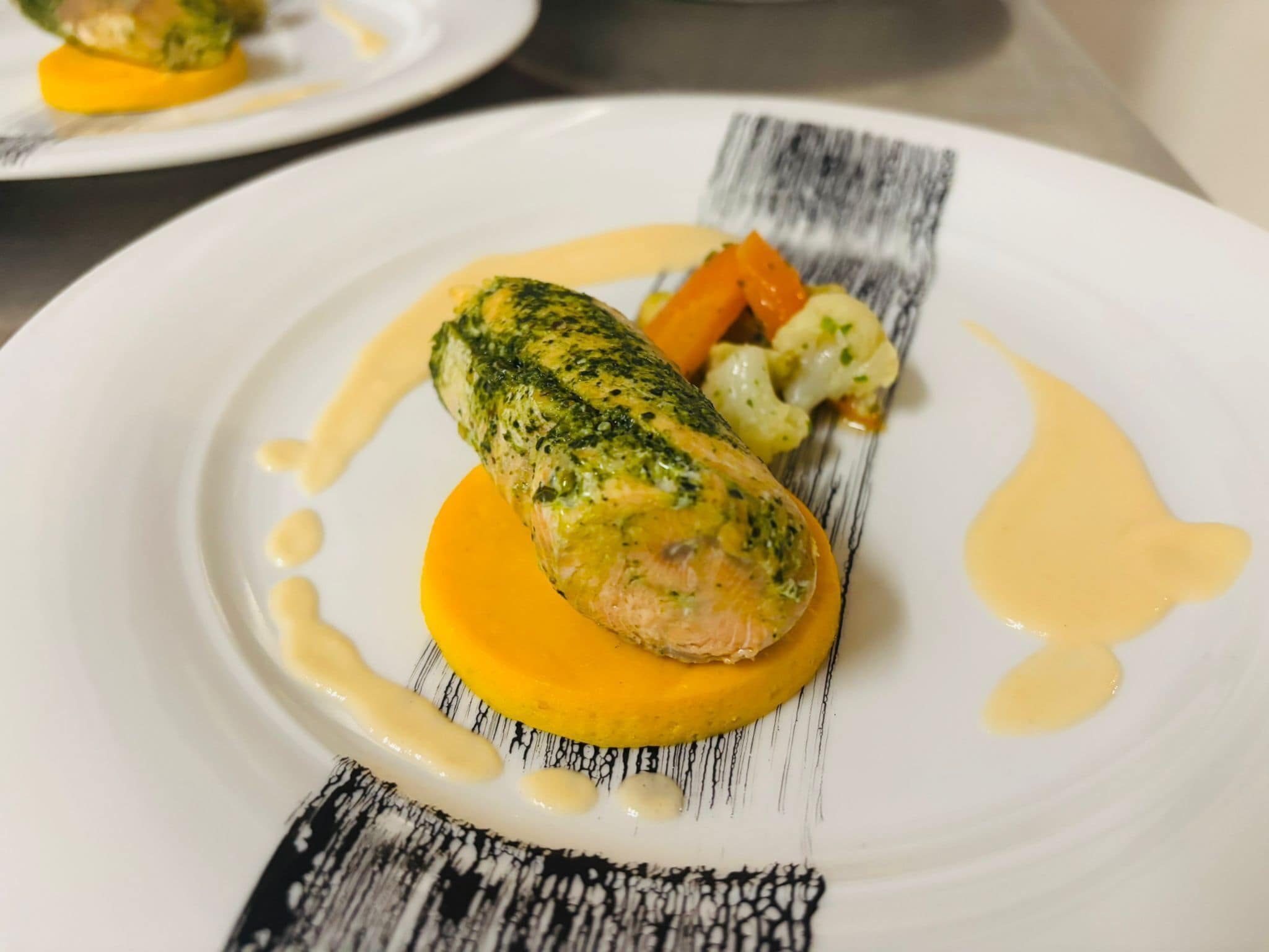 Ein Teller mit Fisch, Gemüse und Soße.