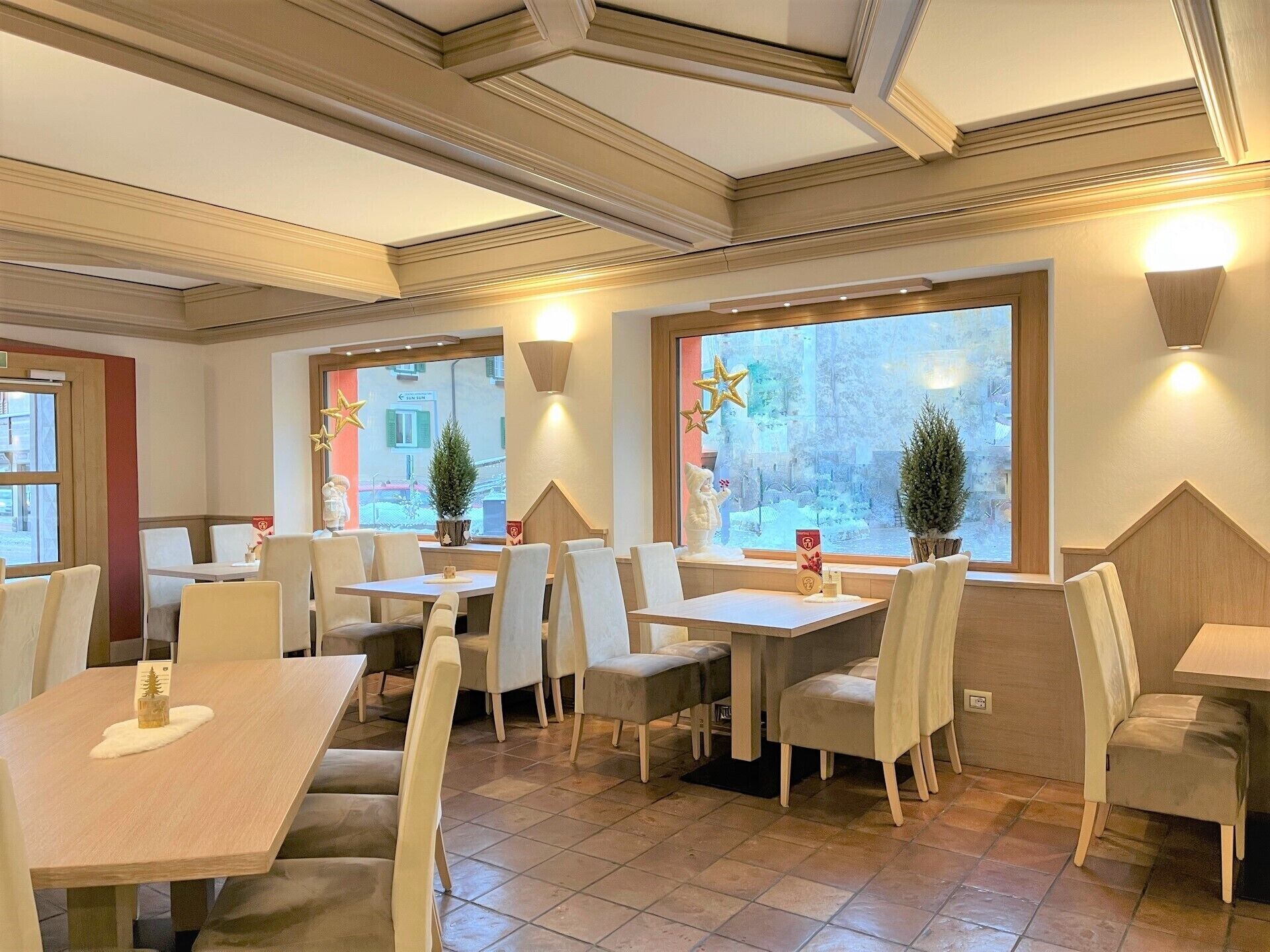 L’intérieur d’un restaurant, avec de nombreuses tables et chaises, de grandes fenêtres agrémentées d’éléments décoratifs et un sol carrelé.