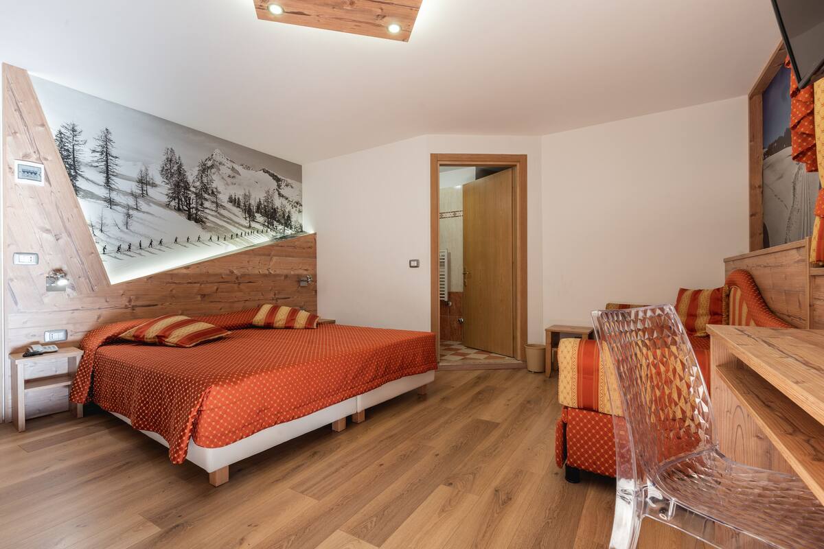 A bedroom with a bed, a chair, a wooden desk, and a painting on the wall.