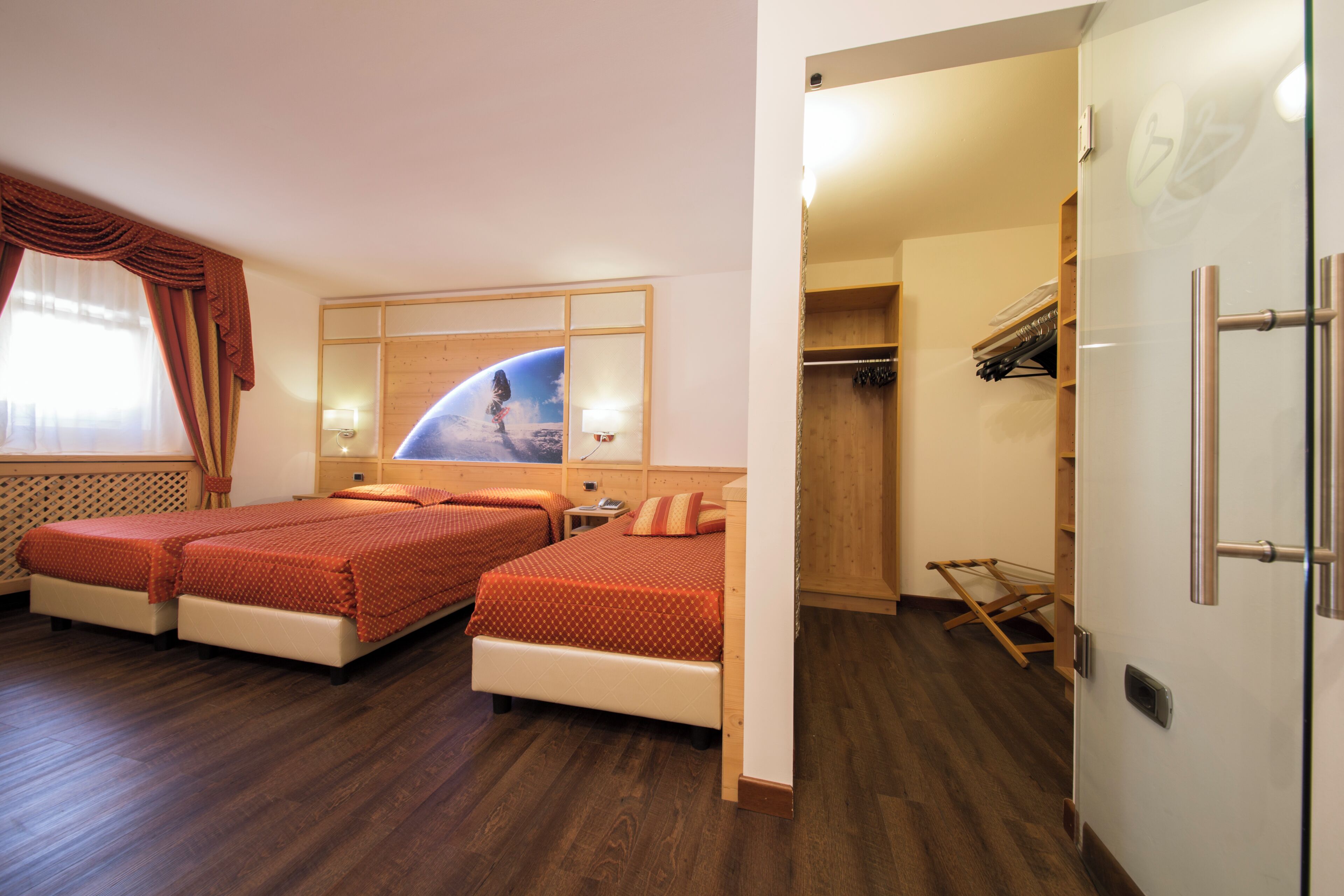 A hotel room with two beds, a wardrobe, and a mirror with a space-themed artwork.