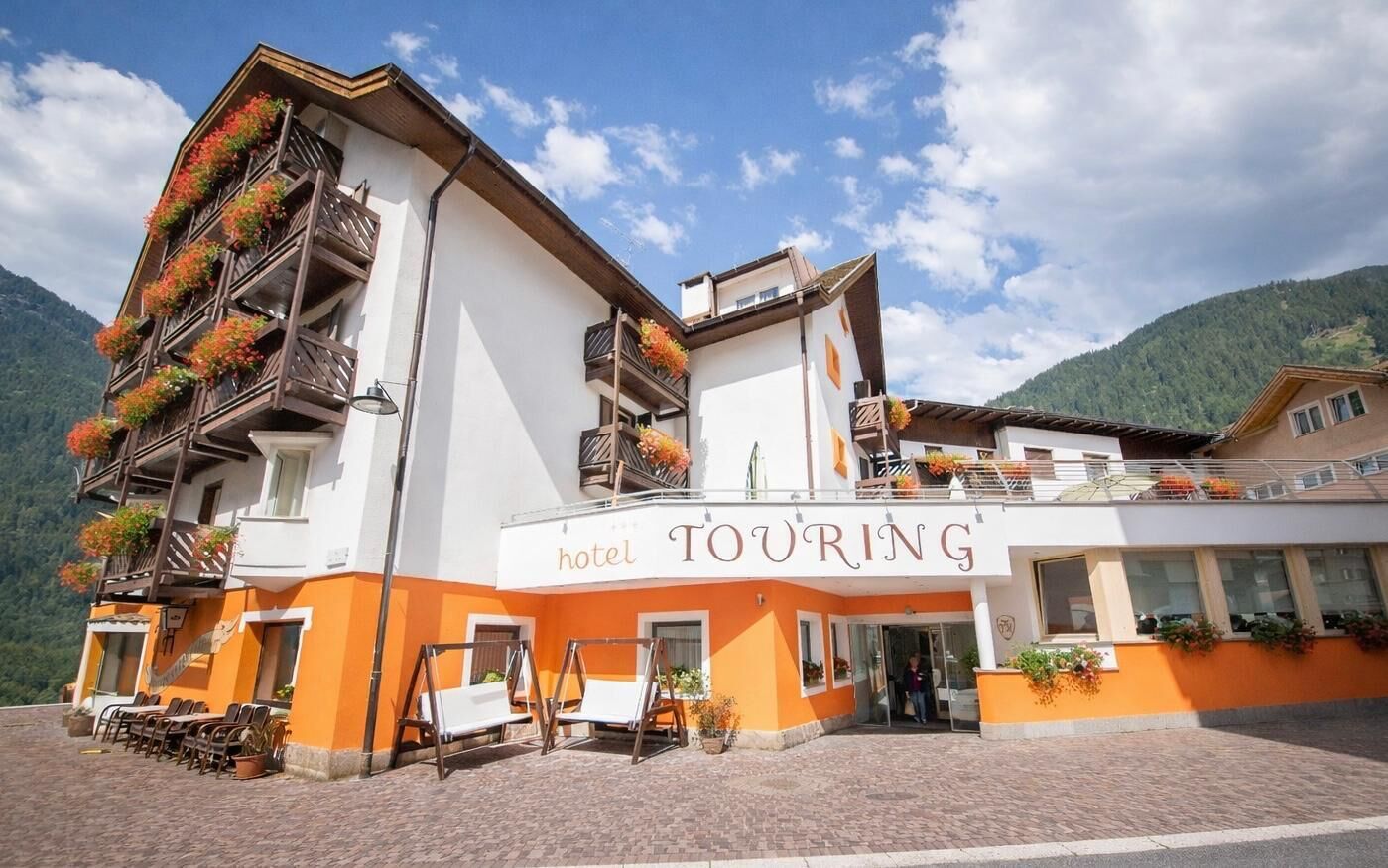 Un hotel con balcones decorados con flores, un letrero que dice 'hotel TOURING' y mobiliario de exterior.