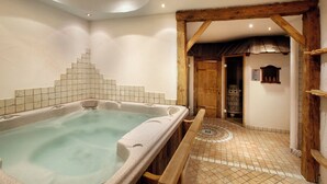 A spa room with a hot tub, wooden beams, tiled floor, and a door leading to another room. - Touring (Predazzo)