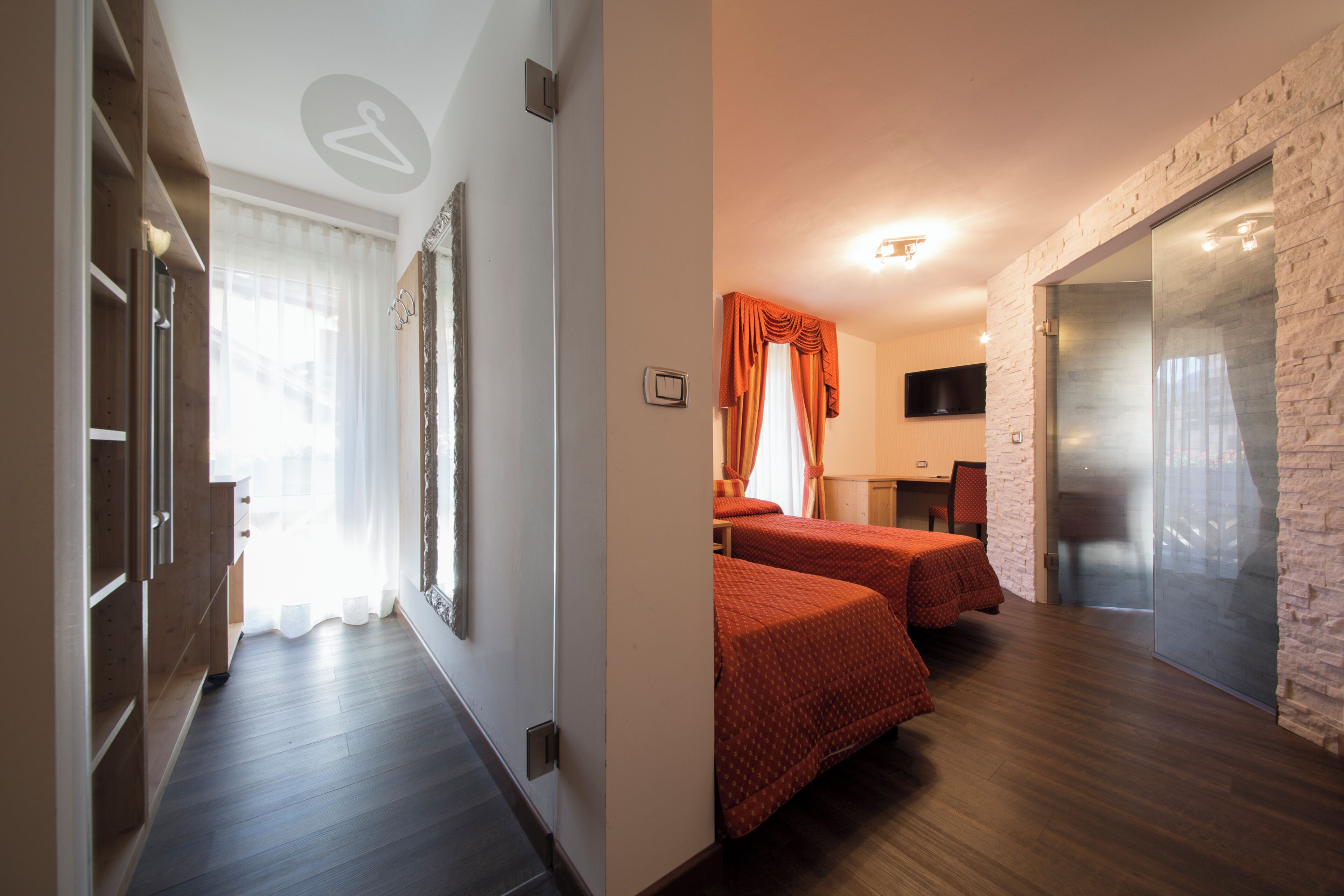 Una habitación de hotel con piso de madera, una cama con cubrecama rojo, un televisor montado en la pared y una pared de acento de ladrillo.