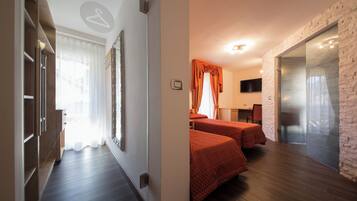 Una habitación de hotel con piso de madera, una cama con cubrecama rojo, un televisor montado en la pared y una pared de acento de ladrillo.