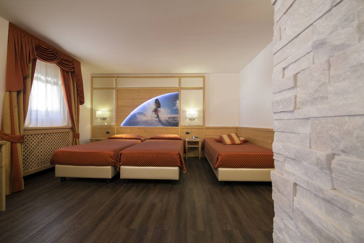 A hotel room with two beds, a wooden headboard, a wall-mounted TV, and a window with curtains.