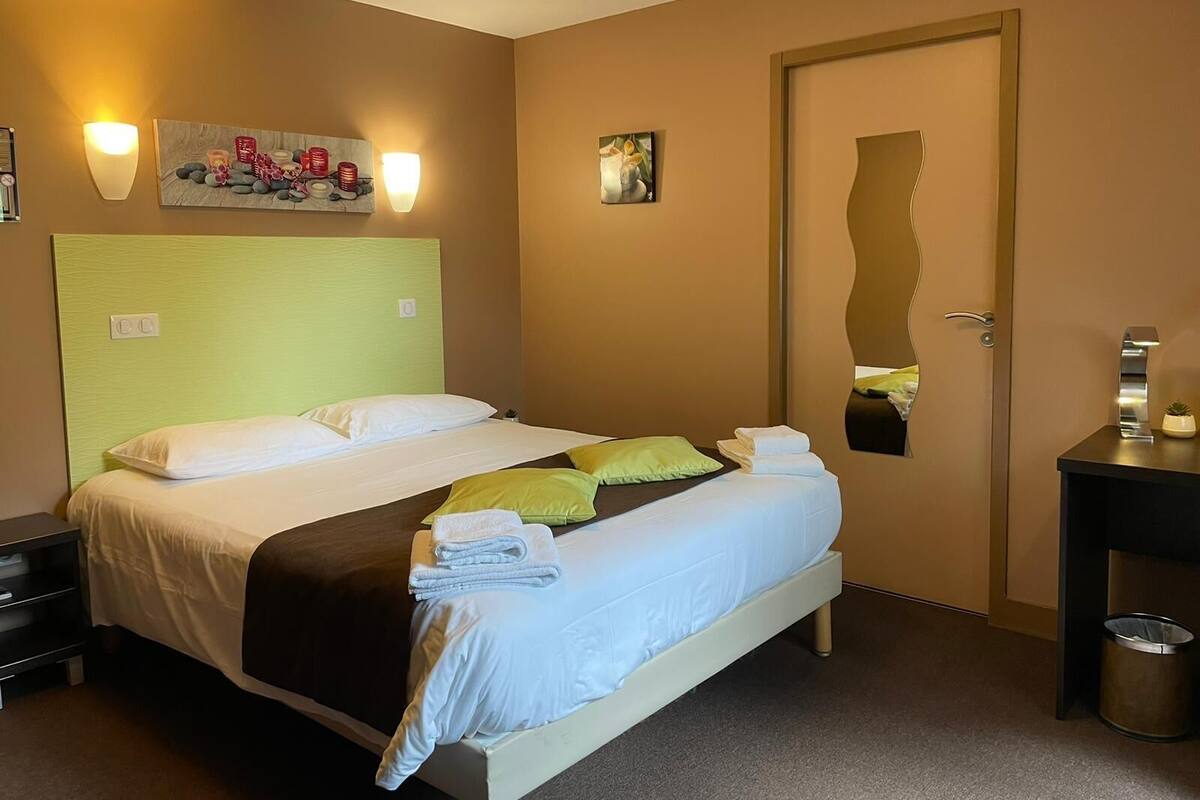 A hotel room with a bed, bedside tables, a trash bin, and artwork on the walls.
