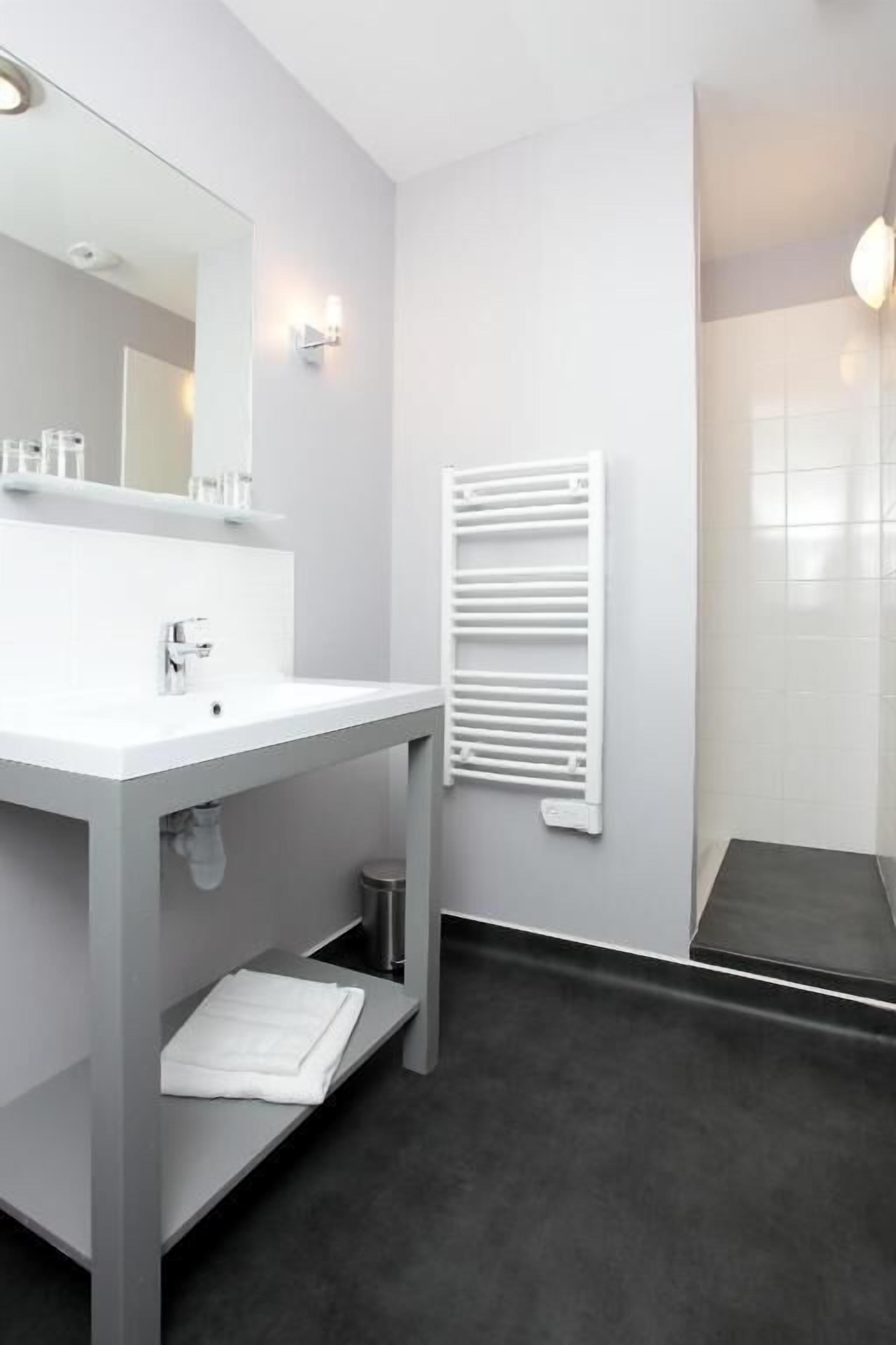 A modern bathroom with a white sink, mirror, and towel rack.