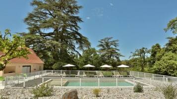 A pool area with lounge chairs and umbrellas, surrounded by a white fence and trees.