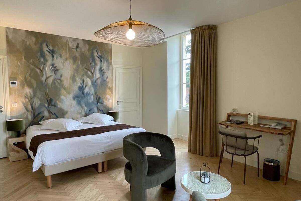 A hotel room with a bed, a desk, a chair, a small table, and a large abstract painting on the wall.