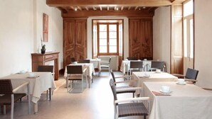 Un comedor con vigas de madera en el techo, mesas con manteles blancos y sillas.