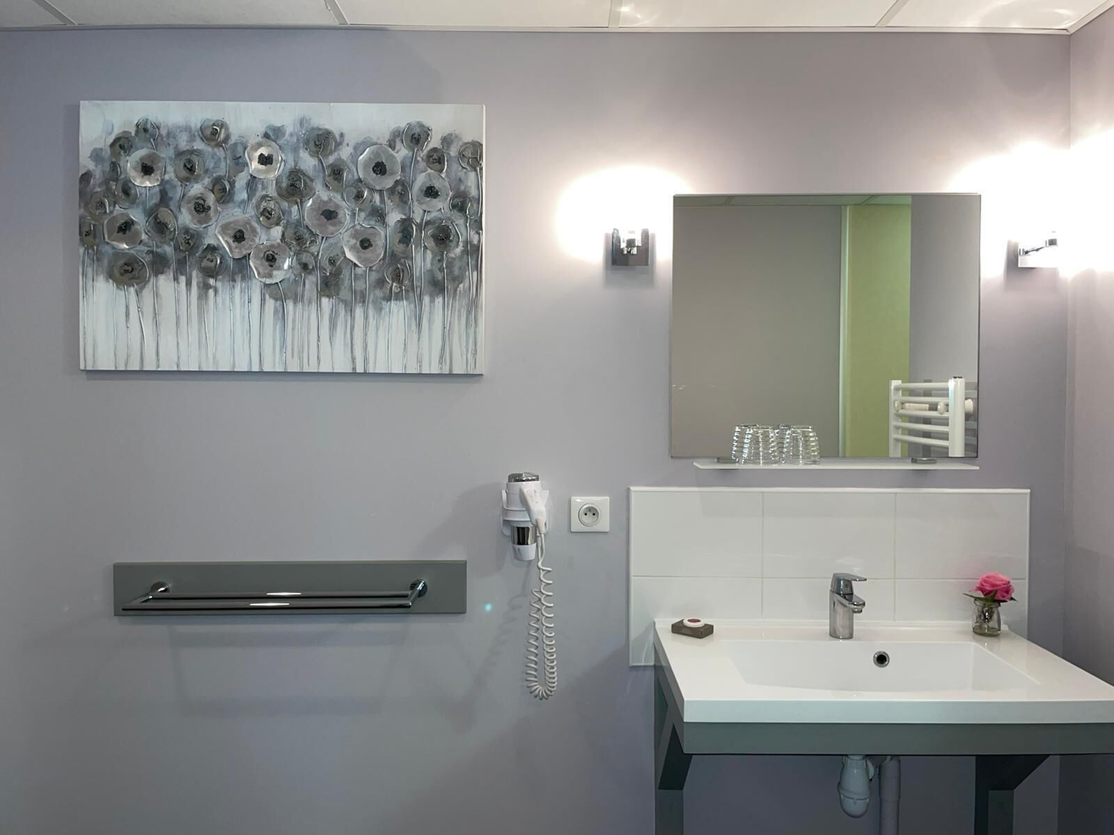 Une salle de bain moderne avec un grand miroir, un lavabo, un porte-serviettes et un sèche-cheveux fixé au mur.