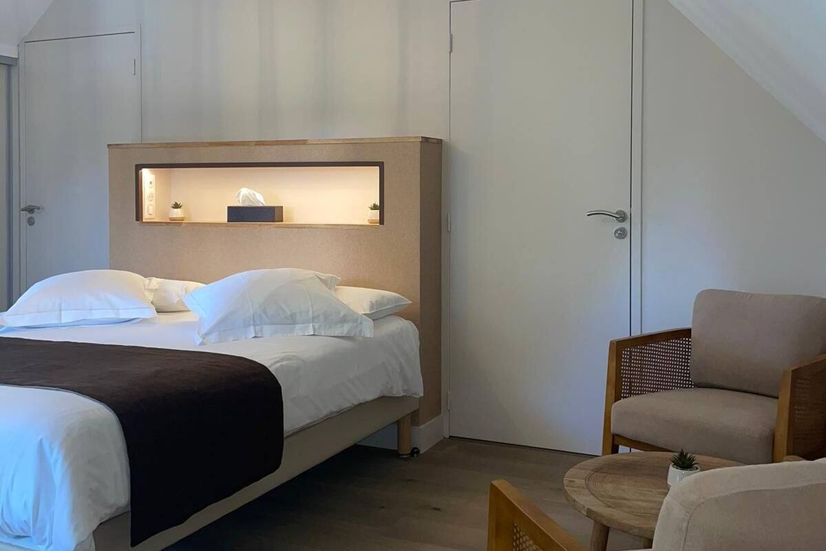 A bedroom with a bed, a chair, a small table, and a ceiling light fixture.
