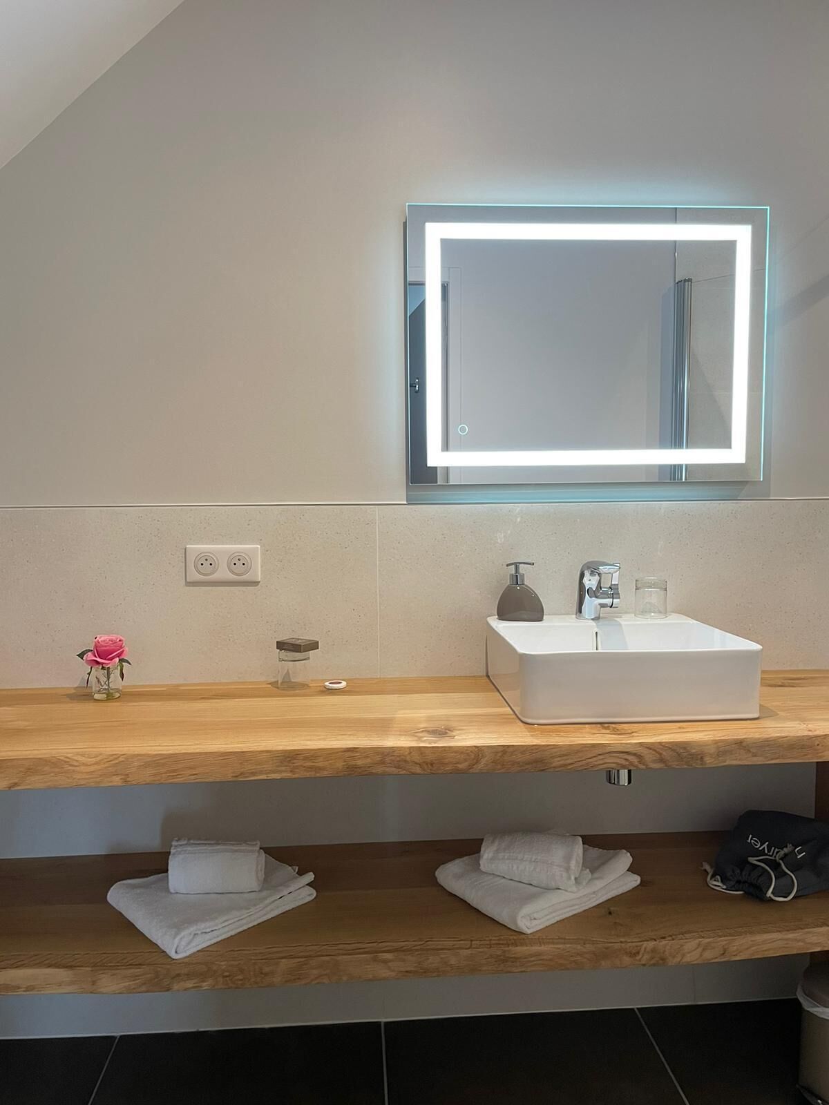 Un baño moderno con un espejo grande, un lavamanos blanco y un tocador de madera.