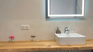 Un baño moderno con un espejo grande, un lavamanos blanco y un tocador de madera.
