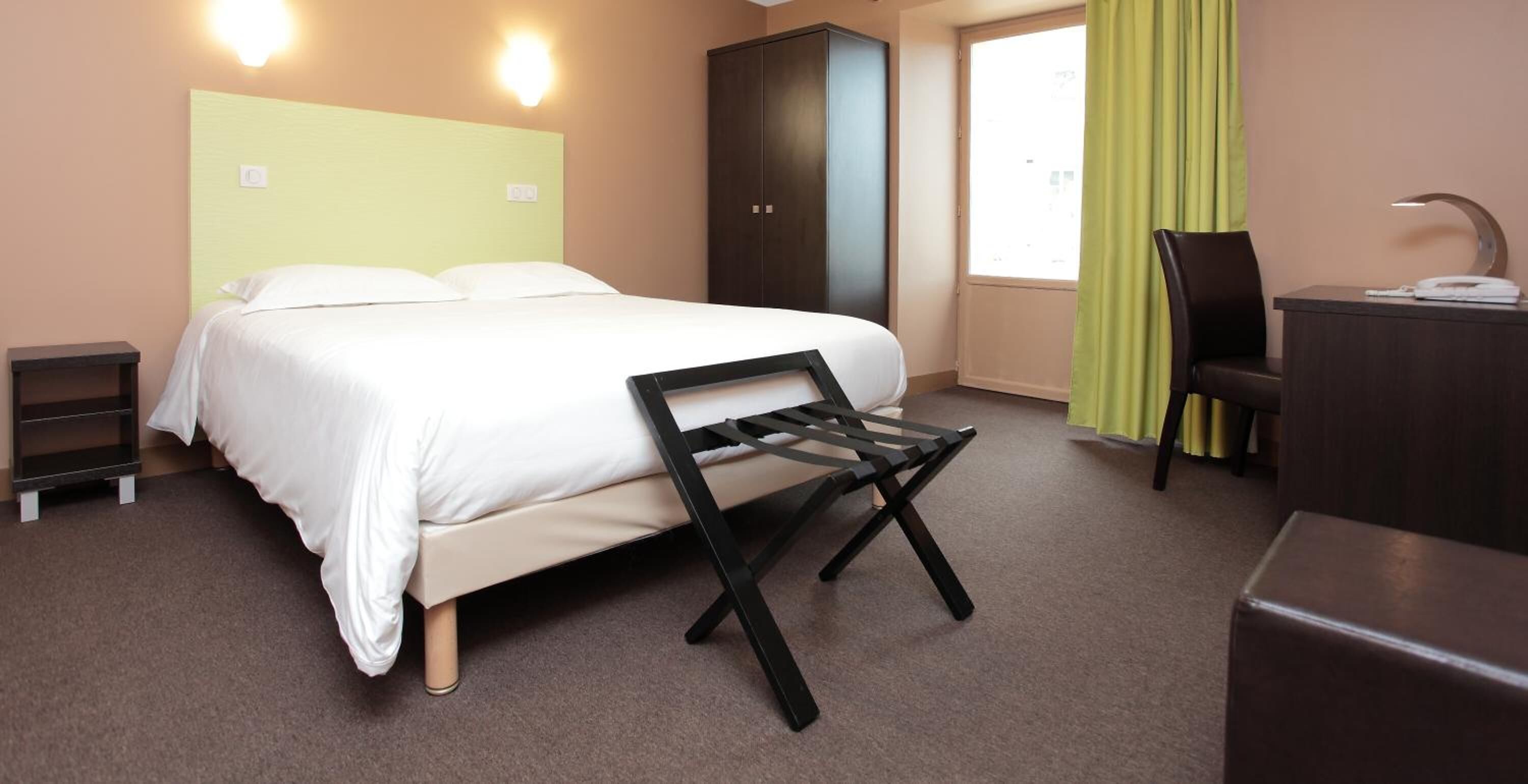 Une chambre d’hôtel avec un lit, un bureau, une chaise et une armoire.