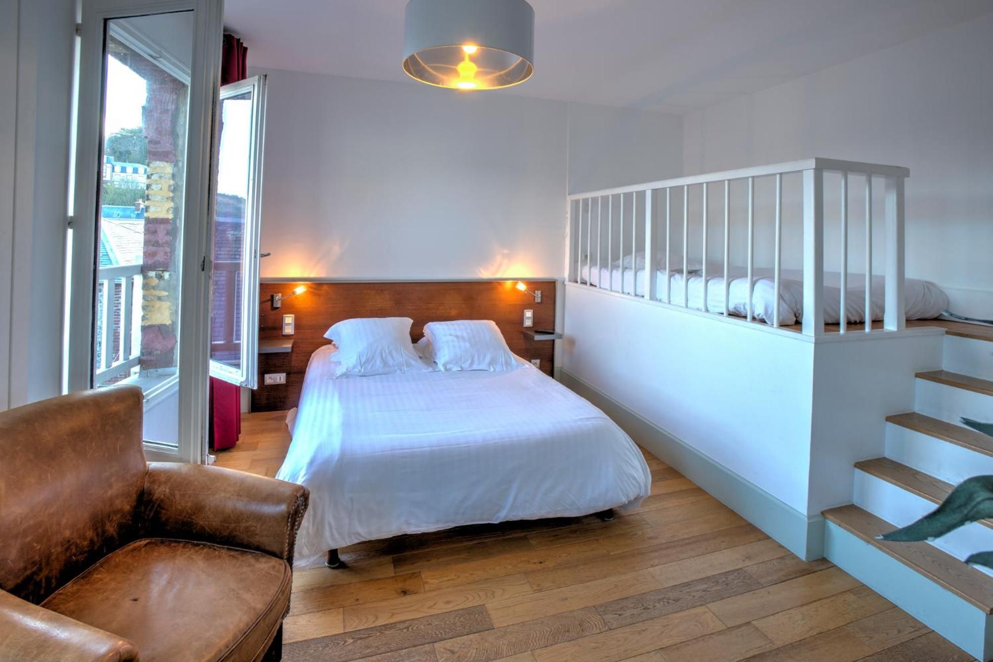 A bedroom with a bed, a chair, a staircase, and a view through a window.