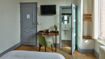 Ein Hotelzimmer mit Bett, Schreibtisch mit Stuhl, Fernseher und einem durch eine offene Tür einsehbaren Badezimmer.