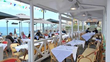 An outdoor dining area with tables and chairs, overlooking the sea.