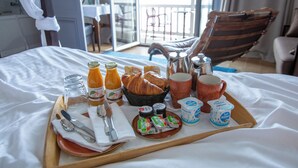 A breakfast tray with croissants, juice, yogurt, and coffee on a bed in a hotel room with a balcony view. - Hotel Le Rayon Vert (Etretat)