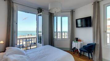 A hotel room with a large bed, a TV, a chair, a small table with a coffee maker, and a balcony with a view of the sea.