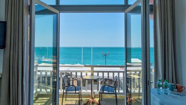 A balcony with a view of the ocean, two chairs, a table, and a bottle of water. - Hotel Le Rayon Vert (Etretat)