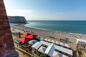 A beachside view with a cliff, umbrellas, and beachgoers. - Hotel Le Rayon Vert (Etretat)