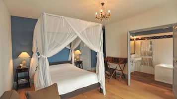 A bedroom with a four-poster bed, bedside lamps, a desk, and a view into the bathroom.