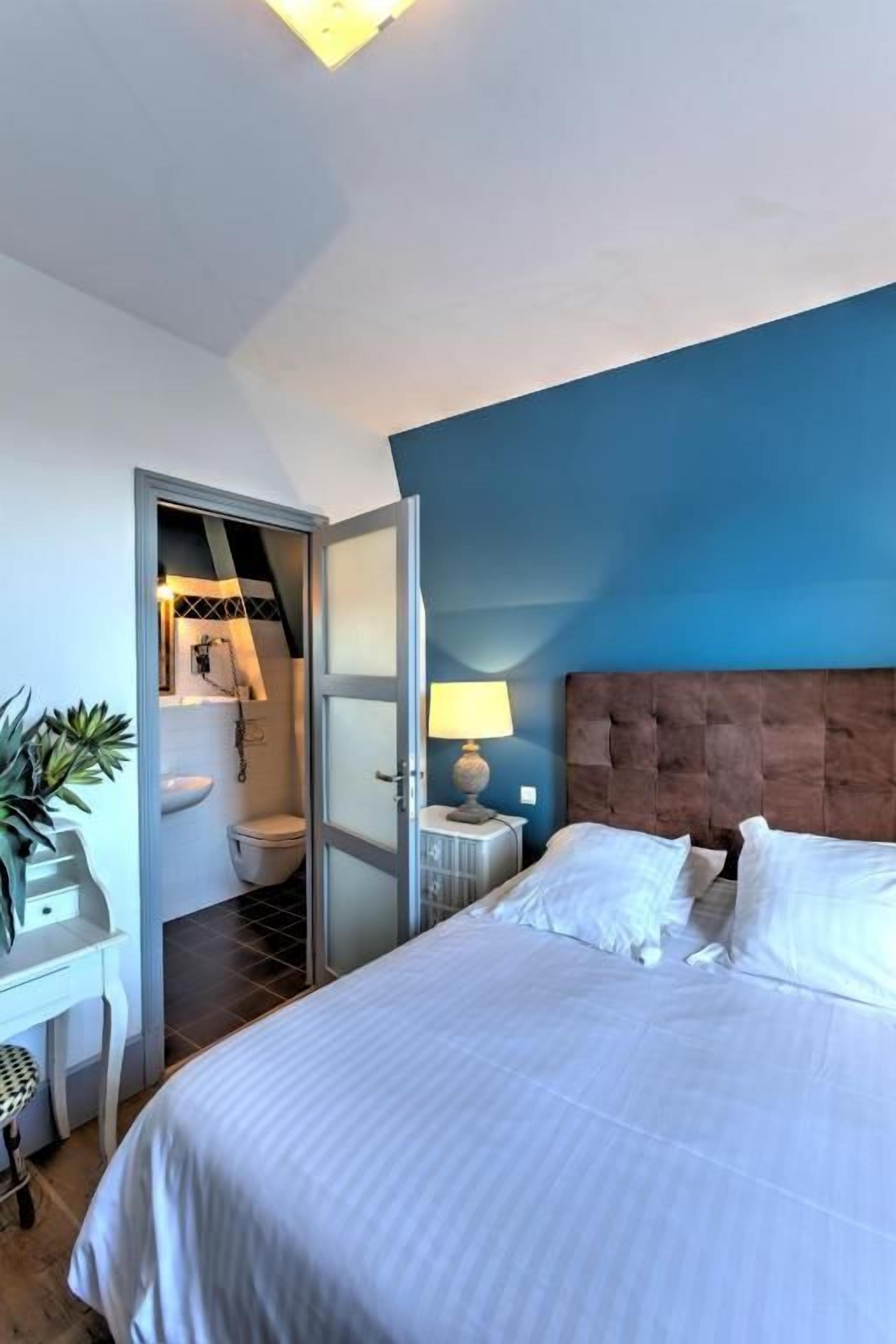 A hotel room with a bed, bedside table, lamp, and a view of the bathroom.