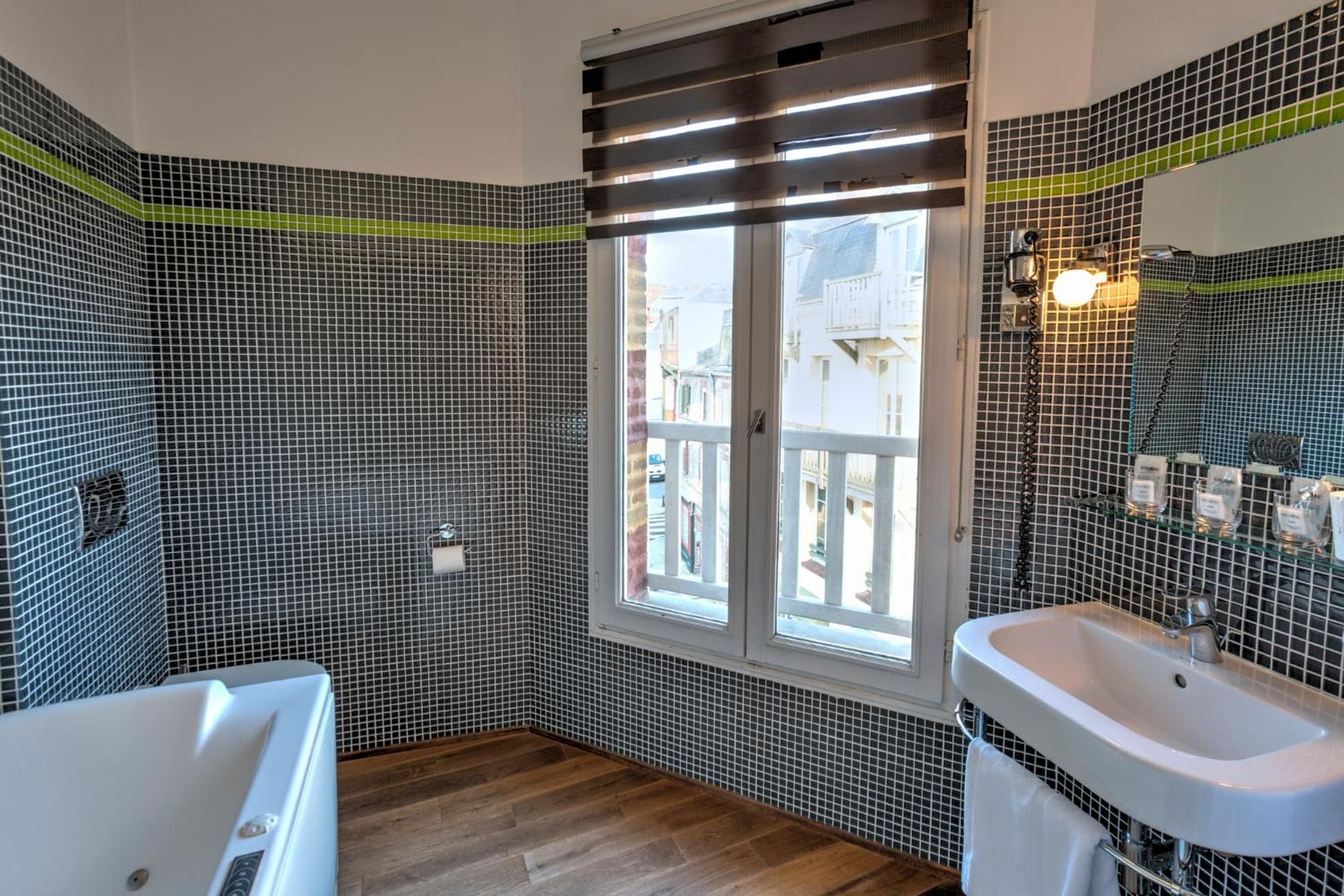 Un baño con bañera, lavamanos y ventana con vistas a edificios.
