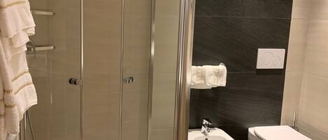 A modern bathroom with a glass-enclosed shower, a bidet, and a white sink.