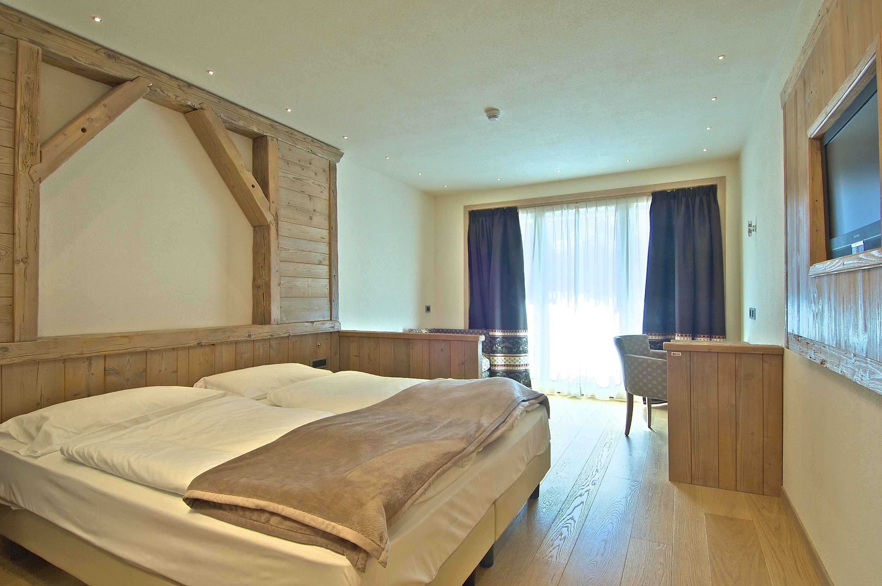 A bedroom with a large bed, wooden headboard, a desk, and a chair.